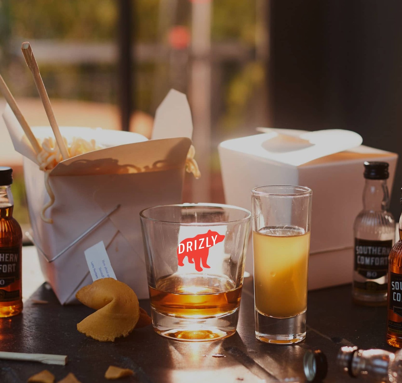 Asian take-out food with Drizly glass and small bottles of Southern Comfort